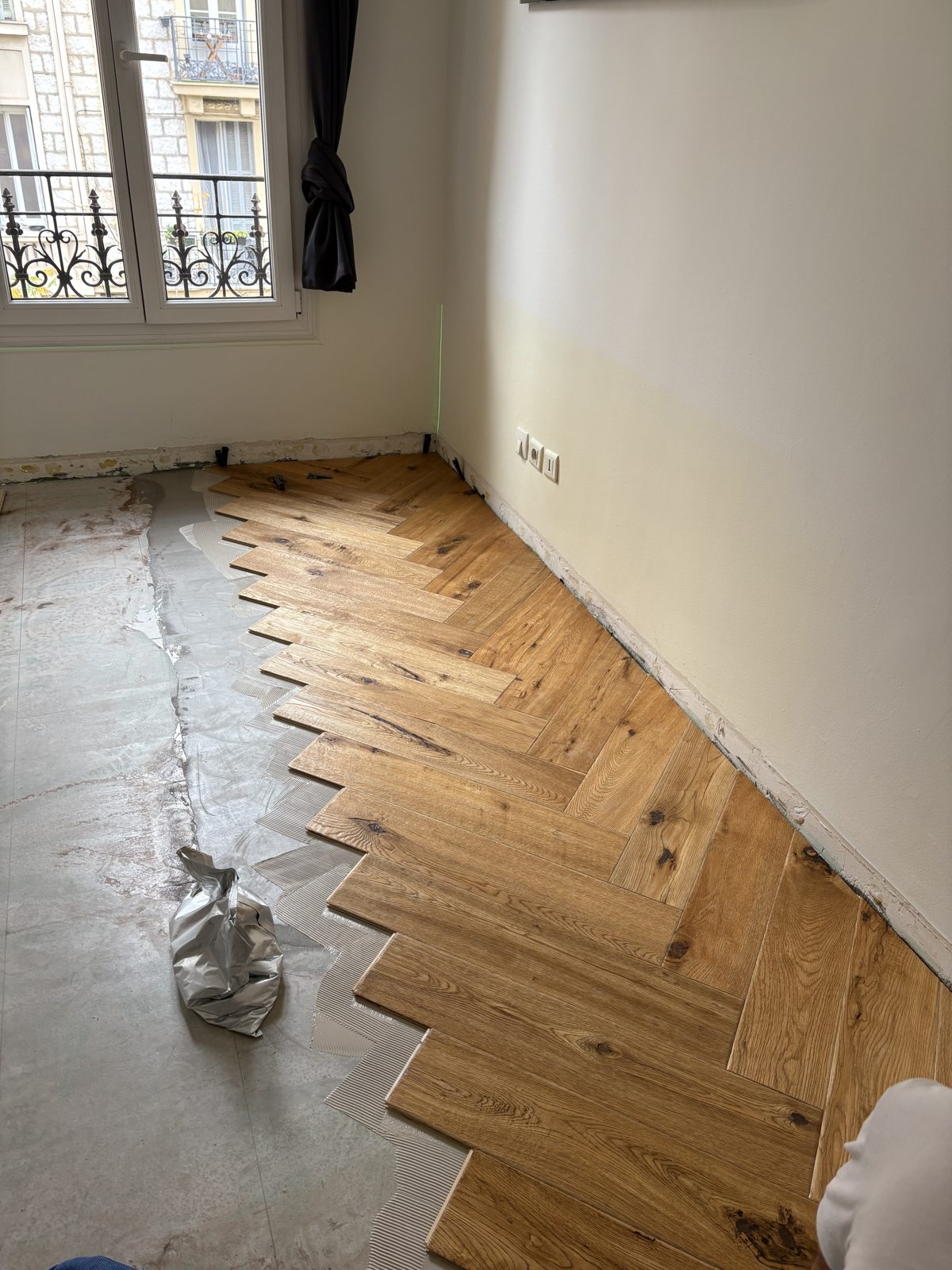 Pose de parquet en bâtons rompus le long d'un axe tracé au laser, colle étalée à la spatule crantée